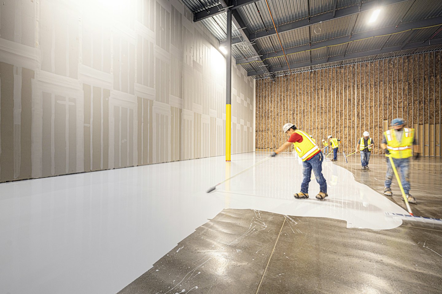 Bouwvakkers brengen witte vloercoating aan in industrieel pand.