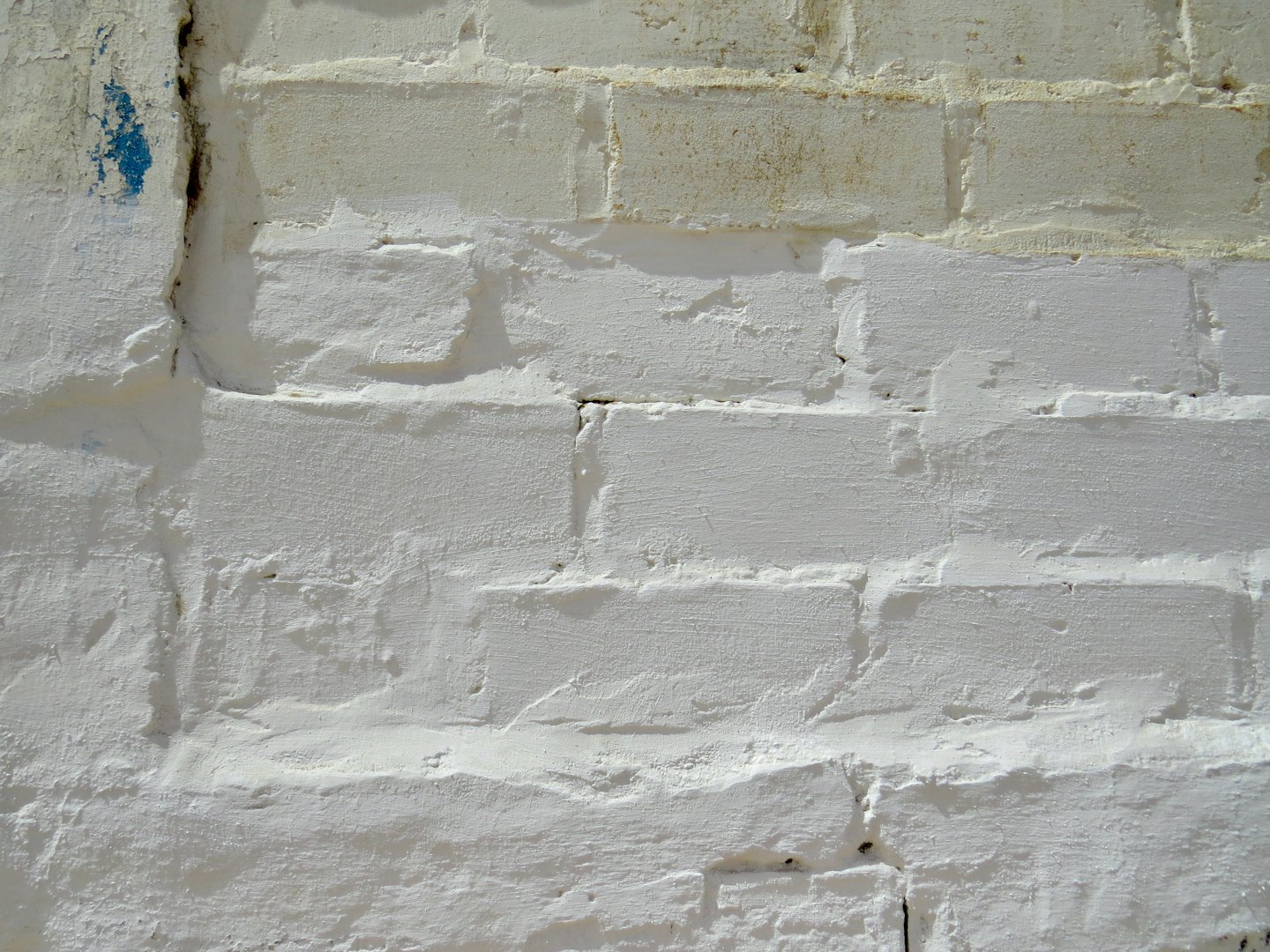 Verweerde witte bakstenen muur met zichtbaar voegwerk en afgebladderde blauwe verf.